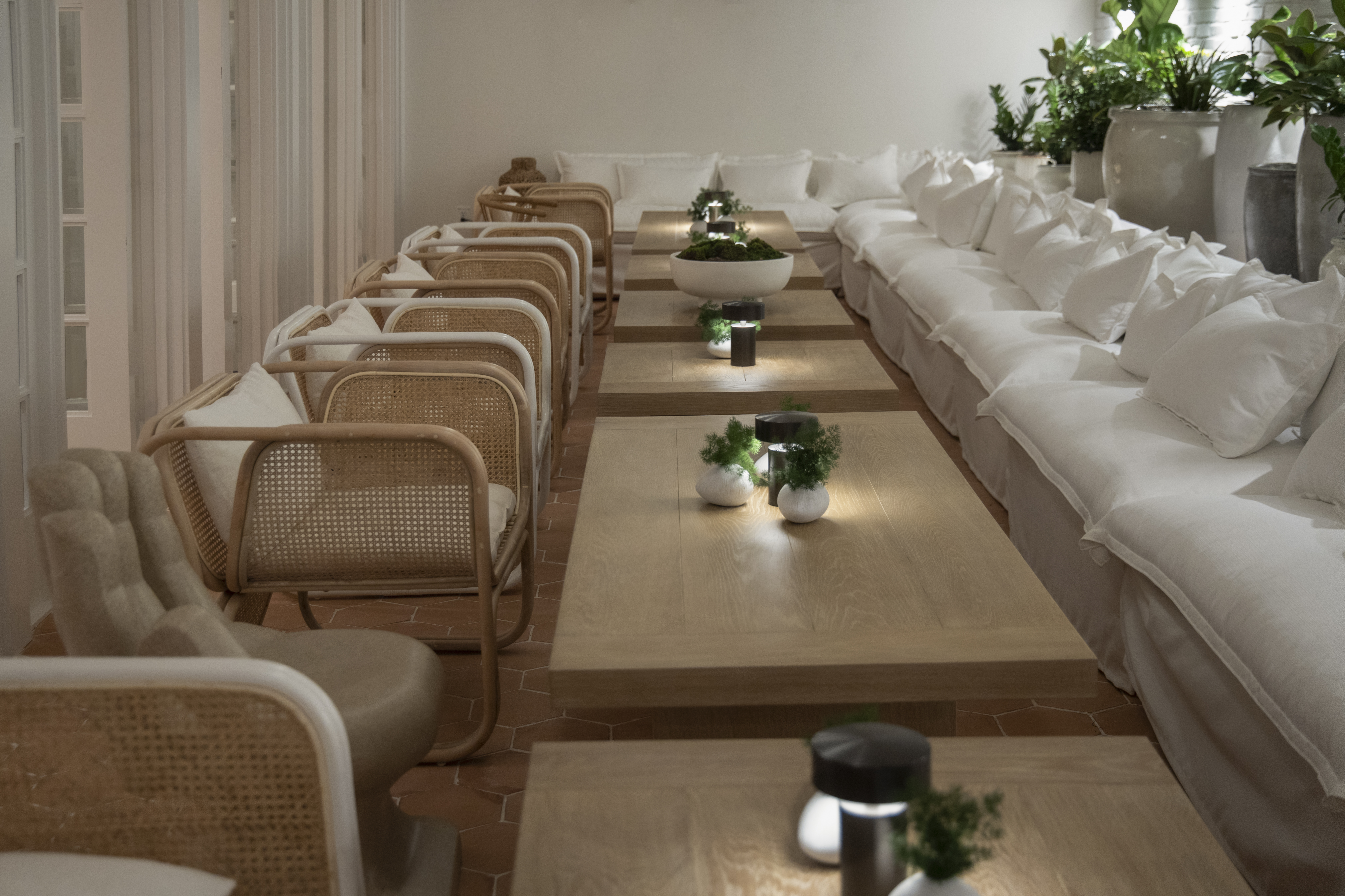 Looking down the long tables in the Conservatory with wooden tables and white seating at Lyle DC.